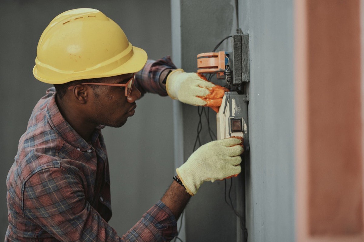 Elektriker mit Schutzhelm und Handschuhen bei der Montage eines Unterputzgeräts an der Wand
