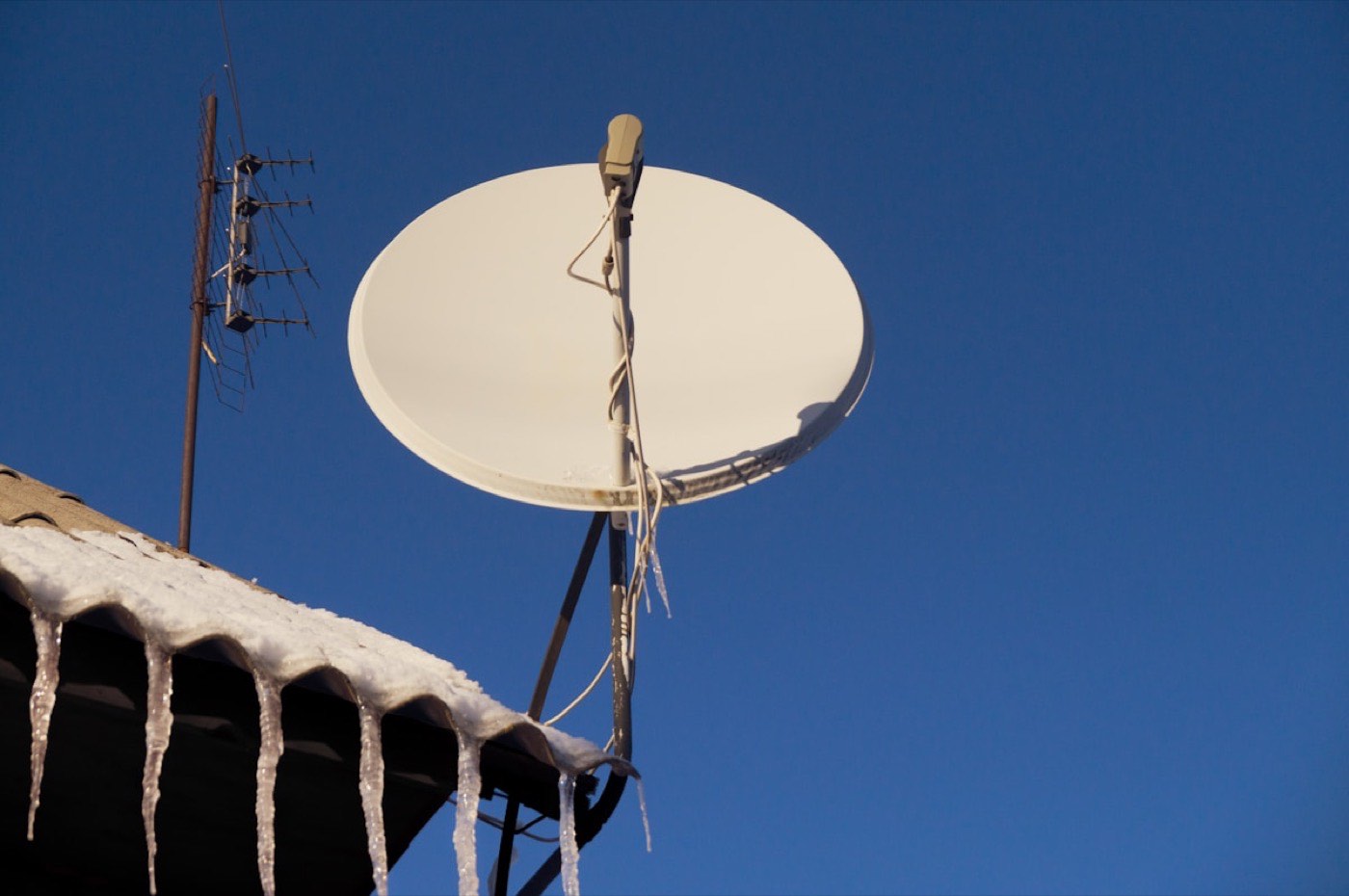 SAT-Schüssel und Dachantenne an einem Hausdach vor klarem Winterhimmel